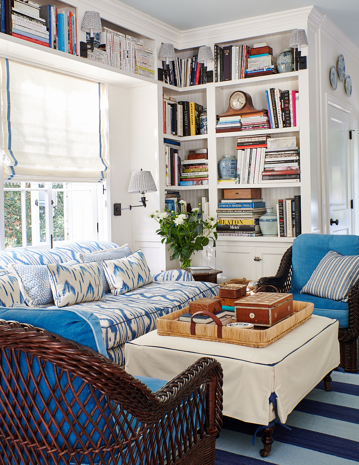 Roman shades, wicker club chairs with turquoise cushions, and cream ottoman with fitted slipcover